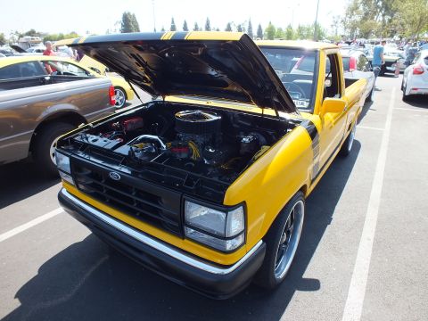 2003 Ford Crown Victoria - yellow Ford Ranger pickup with black hood stripes sits with its hood up at a sunny outdoor car show.
