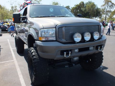2003 Ford Crown Victoria - lifted gray Ford Excursion SUV with a billet grille, three off-road lights and large tires faces the camera at a car show.