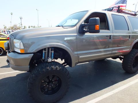 2003 Ford Crown Victoria - lifted gray Ford Excursion Limited SUV with external bypass shocks, black wheels and mud tires sits at an outdoor show.