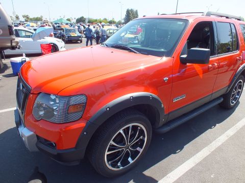 2003 Ford Crown Victoria - orange Ford Explorer SUV with black fender flares and machined-spoke wheels sits in a packed car-show parking lot.