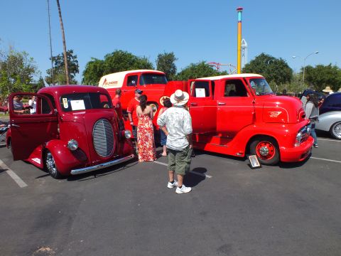 2003 Ford Crown Victoria - Two restored vintage red Ford cab-over-engine trucks draw onlookers at a sunny outdoor classic-truck show.