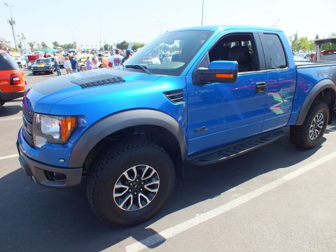 2003 Ford Crown Victoria - blue Ford F-150 SVT Raptor extended cab with fender flares and off-road tires parks among rows of cars at a show.