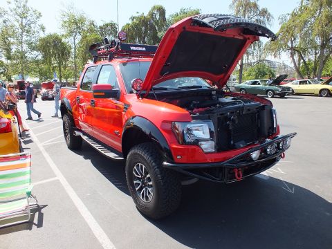 2003 Ford Crown Victoria - red and black Ford Raptor crew cab with a Yakima roof rack, light bar and open hood sits on display at an outdoor car show.