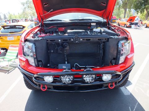 2003 Ford Crown Victoria - Head-on view of a red pickup with the hood raised, revealing the radiator core support and a bumper-mounted KC driving-light bar.