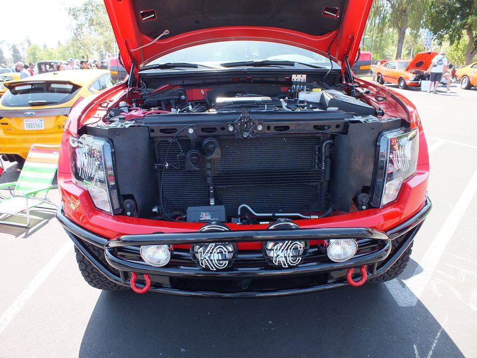 Front view of a red truck with hood up showing radiator core support and KC light bar
