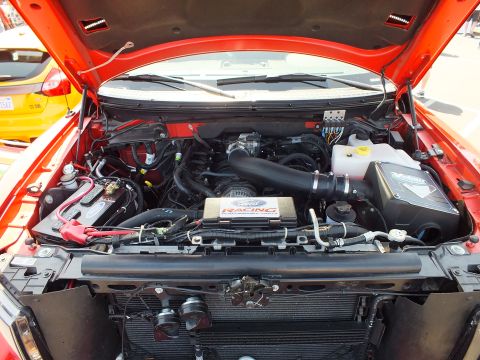2003 Ford Crown Victoria - engine bay of a red truck showing a black Ford Racing cold-air intake, coolant reservoir, and battery under the raised hood.