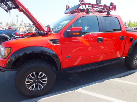 2003 Ford Crown Victoria - Side profile of a red Ford F-150 SVT Raptor crew cab showing a 6.2L fender badge, black wheel arches, and a roof basket rack.