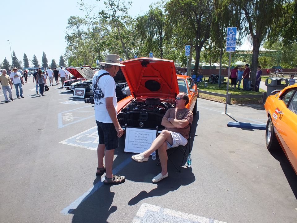 Orange coupe with raised hood and display placard, men talking at a car show
