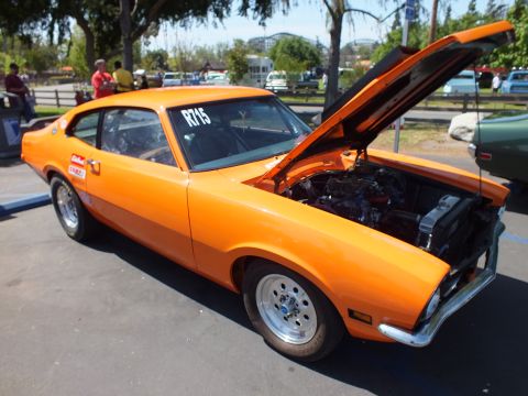 2003 Ford Crown Victoria - orange Ford Maverick two-door coupe on slotted mag wheels with its hood and trunk open and racing decals, parked at an outdoor show.