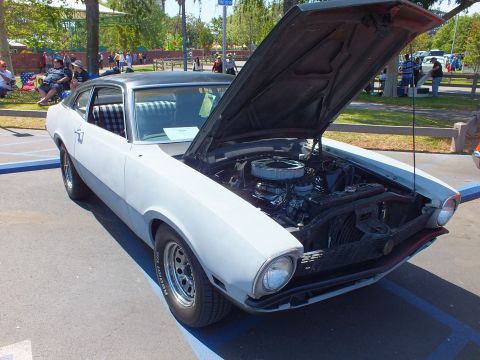 2003 Ford Crown Victoria - white Ford Maverick coupe with a black vinyl roof and its hood raised showing the engine, parked among spectators at a show.