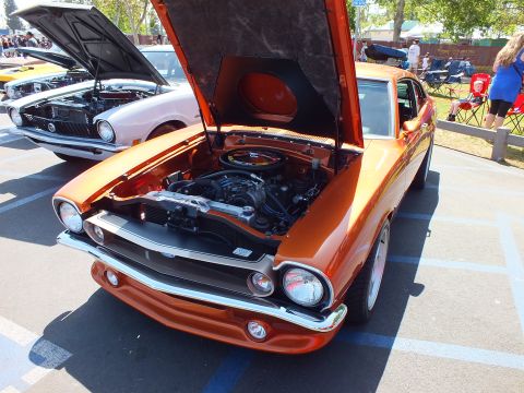 2003 Ford Crown Victoria - glossy burnt-orange compact muscle car sits with its hood raised at a sunny car show, chrome bumper and round headlights gleaming.