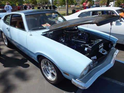 2003 Ford Crown Victoria - light-blue Ford Maverick with a carbon-fiber hood propped open shows its engine while parked at a busy car show.