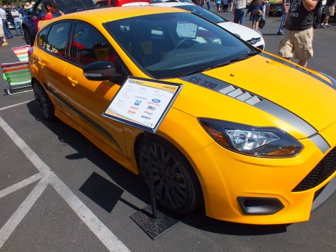 2003 Ford Crown Victoria - Side view of a yellow Ford Focus hatchback with gray stripes, black wheels and an information placard at an outdoor car show.