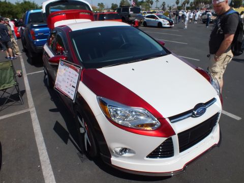 2003 Ford Crown Victoria - two-tone red-and-white Ford Focus sedan with a printed display card is parked among vehicles at a sunny car show.