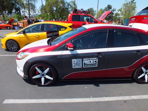 2003 Ford Crown Victoria - Close side view of a Ford Focus hatchback showing a 'Watch Season 1 Project Vehicle' QR-code decal and red-lip alloy wheels.