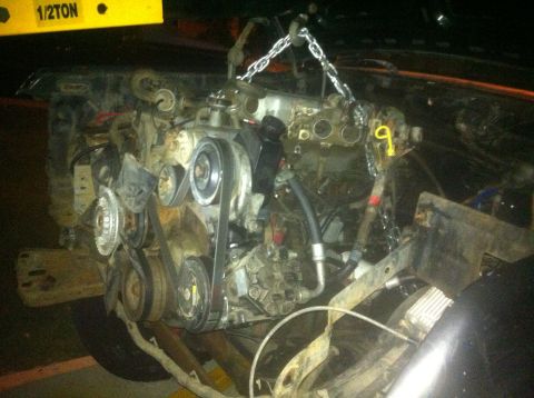 1989 Ford Bronco - Engine removal in progress, supported by a chain hoist. Yellow 1/2 TON label is visible.
