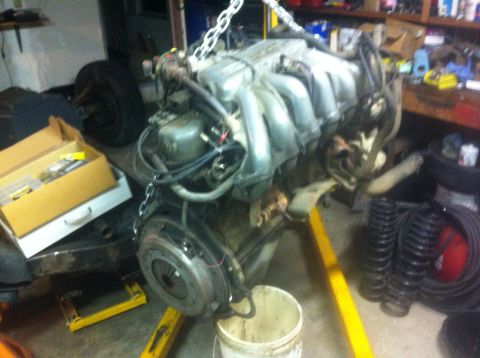 1989 Ford Bronco - An engine and transmission assembly is suspended by chains in a workshop setting, with various parts and tools visible.