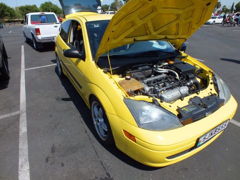 2003 Ford Crown Victoria - yellow Ford Focus three-door coupe with its hood raised, exposing the engine bay, parked at an outdoor car show.