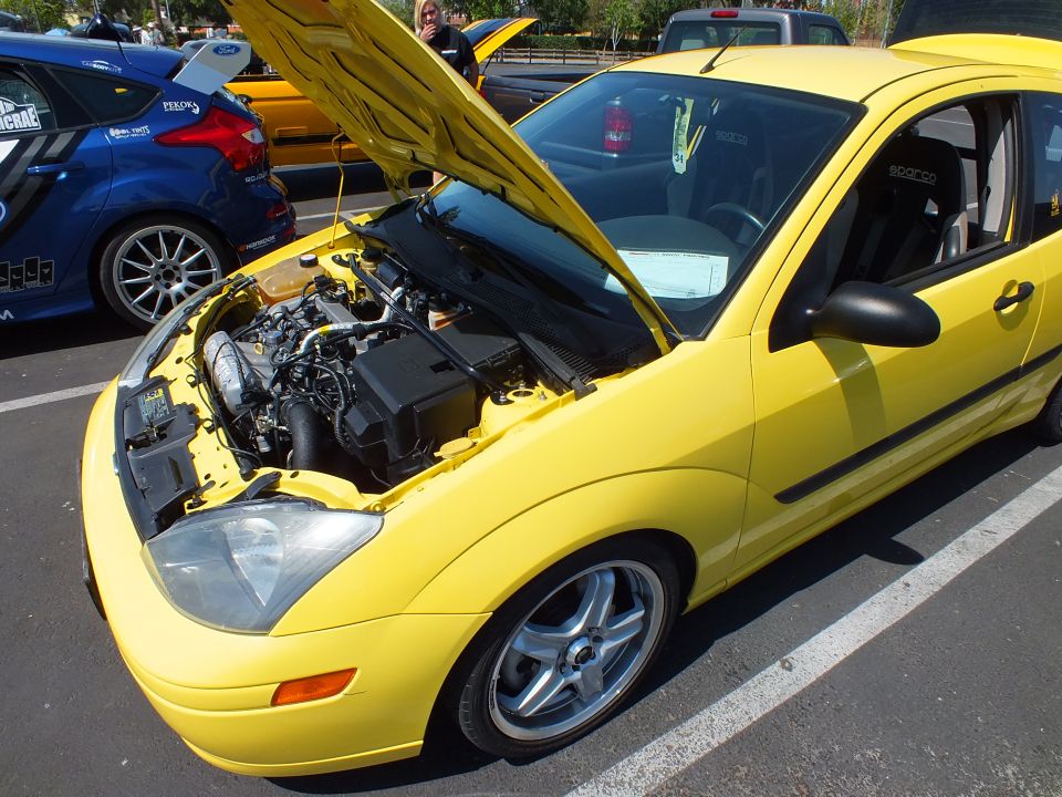 Yellow Ford Focus coupe with hood open at a car show