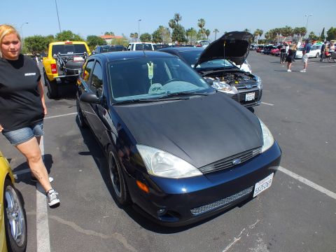 2003 Ford Crown Victoria - dark blue Ford Focus with a debadged smoothed front end and black wheels parked at a crowded outdoor car show.