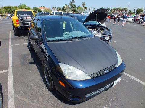 2003 Ford Crown Victoria - Front three-quarter view of a dark blue Ford Focus hatchback with black wheels parked among show cars in a lot.