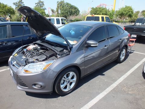 2003 Ford Crown Victoria - gray Ford Focus sedan with its hood open displaying the engine bay, parked in a lot with a roller coaster visible behind.