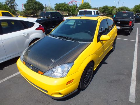 2003 Ford Crown Victoria - bright yellow Ford Focus SVT hatchback with a carbon-fiber hood and black wheels parked at an outdoor car meet.