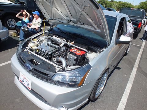 2003 Ford Crown Victoria - silver Ford Focus sedan with hood raised and doors open at a car show, with onlookers seated nearby.