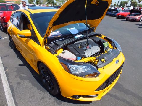 2003 Ford Crown Victoria - yellow Ford Focus hatchback with its hood raised, revealing the engine bay, parked at a sunny car show.