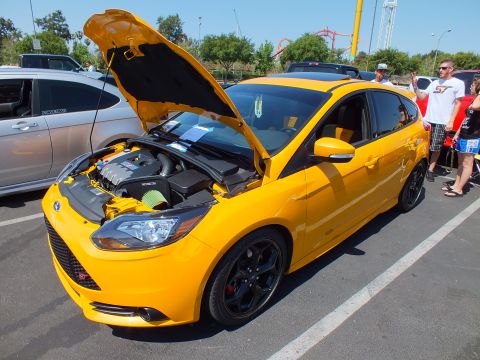 2003 Ford Crown Victoria - yellow Ford Focus ST hatchback with its hood raised and black wheels, with spectators standing beside it.