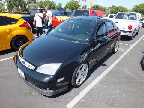 2003 Ford Crown Victoria - lowered black Ford Focus sedan with silver alloy wheels parked among other cars at an outdoor show.