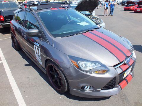 2003 Ford Crown Victoria - gray Ford Focus hatchback with red center racing stripes, roof rack, and number 12 door decals at a car show.