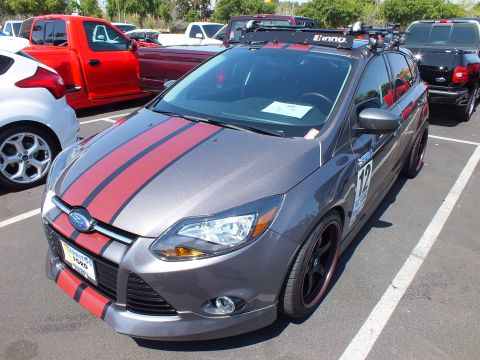 2003 Ford Crown Victoria - gray Ford Focus hatchback with red racing stripes, black-and-red wheels, and a roof rack at a car show.