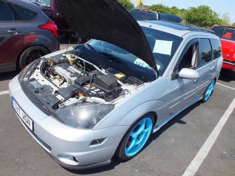2003 Ford Crown Victoria - silver Ford Focus wagon with hood raised, lowered stance, and blue wheels, plate SVT WGN, at a car show.
