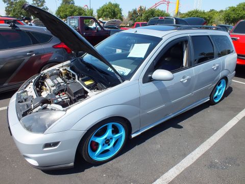 2003 Ford Crown Victoria - silver Ford Focus wagon with its hood raised, blue wheels with red calipers, and roof rails at an outdoor meet.
