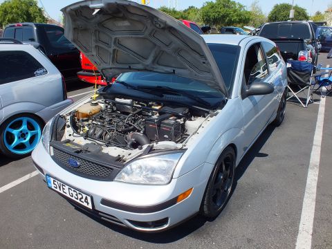 2003 Ford Crown Victoria - silver Ford Focus with black alloy wheels has its hood open displaying the engine bay in a sunny parking lot.