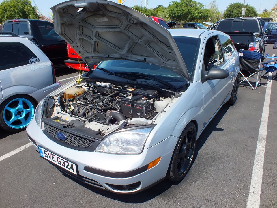 Silver Ford Focus with hood up showing engine, black wheels, at outdoor show