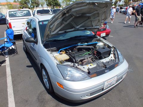 2003 Ford Crown Victoria - silver Ford Focus hatchback shows its engine bay with hood up, parked among cars near a Ford-bannered truck.