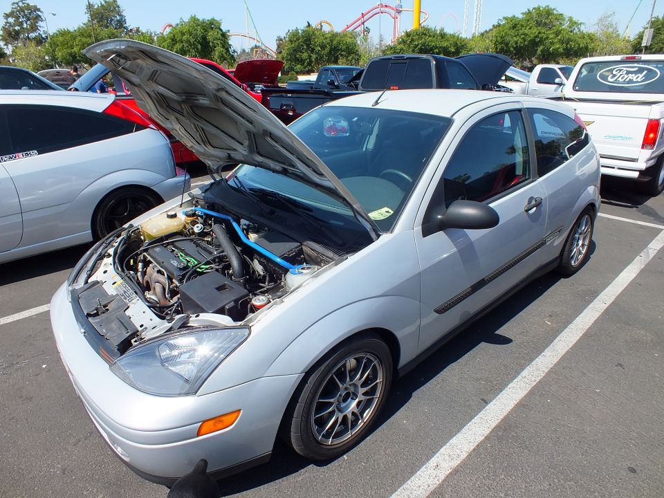 Silver Ford Focus two-door hatchback with hood open, roller coaster behind