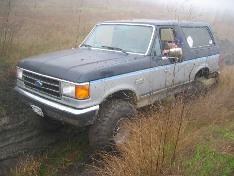 1989 Ford Bronco - A two-tone Ford Bronco navigates a muddy terrain with its off-road tires.