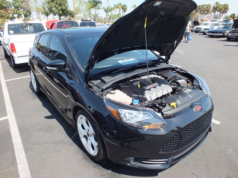 Black Ford Focus ST hatchback with hood open showing engine at car show