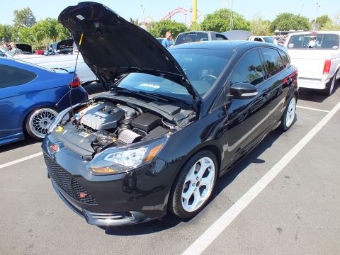 2003 Ford Crown Victoria - glossy black Ford Focus ST hatchback shows its engine bay with hood raised, parked at an outdoor car show.