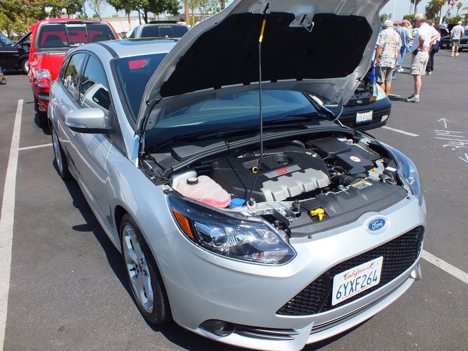 Silver Ford Focus ST sedan with hood open showing engine at a car show