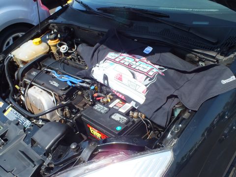 2003 Ford Crown Victoria - car engine bay with blue spark-plug wires and a graphic black T-shirt laid across the battery and intake.