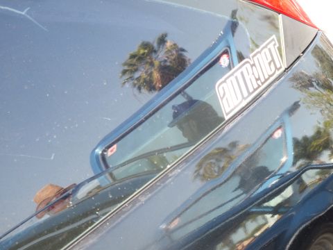 2003 Ford Crown Victoria - dark blue car hood reflects palm trees and onlookers, with a supermotors.net sticker applied near the edge.
