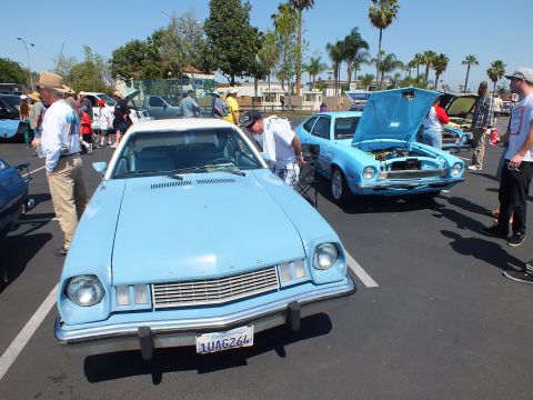 2003 Ford Crown Victoria - light blue Ford Pinto with a white roof faces the camera amid a crowd at a sunny parking-lot car show.