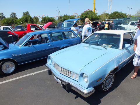2003 Ford Crown Victoria - light blue Ford Pinto with a white top sits beside a blue Pinto wagon at a crowded outdoor car show.