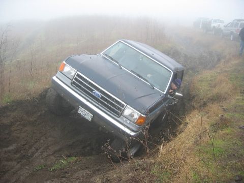 1989 Ford Bronco - Ford Bronco stuck in a muddy ditch with other vehicles visible in the fog.
