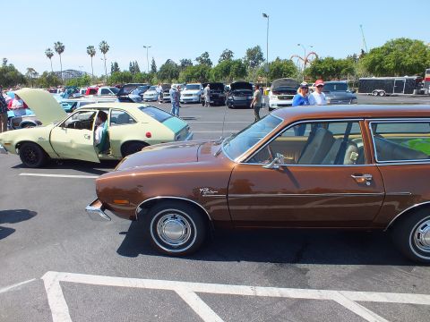 2003 Ford Crown Victoria - brown Ford Pinto wagon sits in the foreground with a pale yellow hatchback parked behind it at a crowded car show.