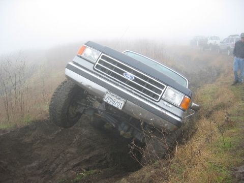 1989 Ford Bronco - A Ford truck navigates a muddy incline with other vehicles visible in the foggy distance.